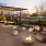 a fire pit and a deck with chairs and a building in the background